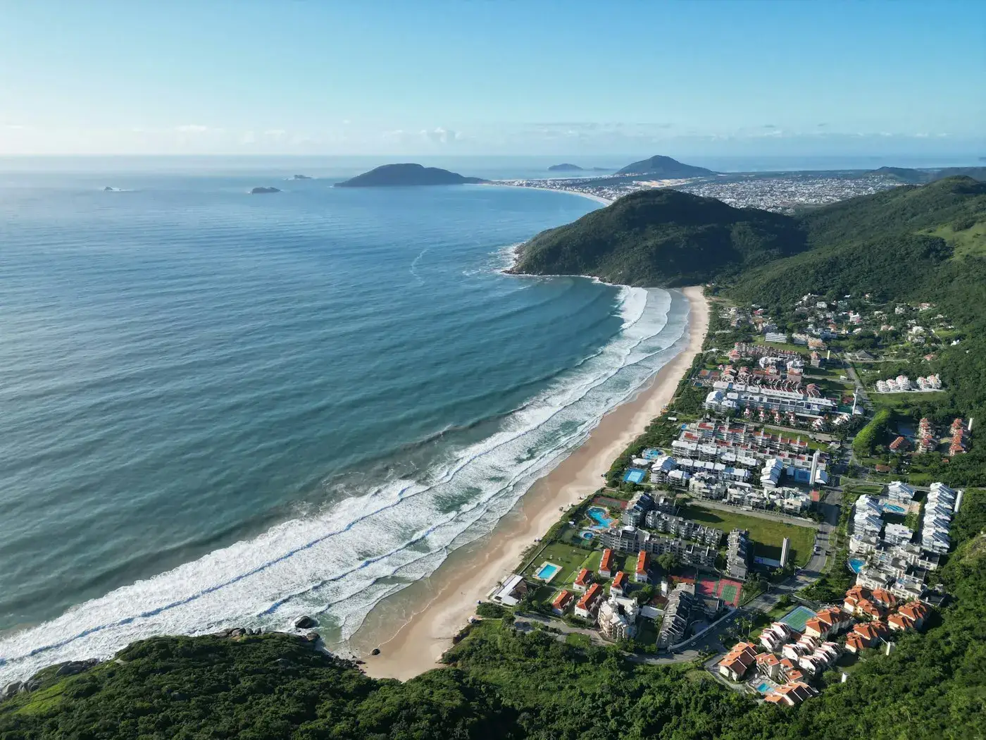 Vista aérea de praia com ondas e bairro planejado à beira-mar no norte da Ilha
