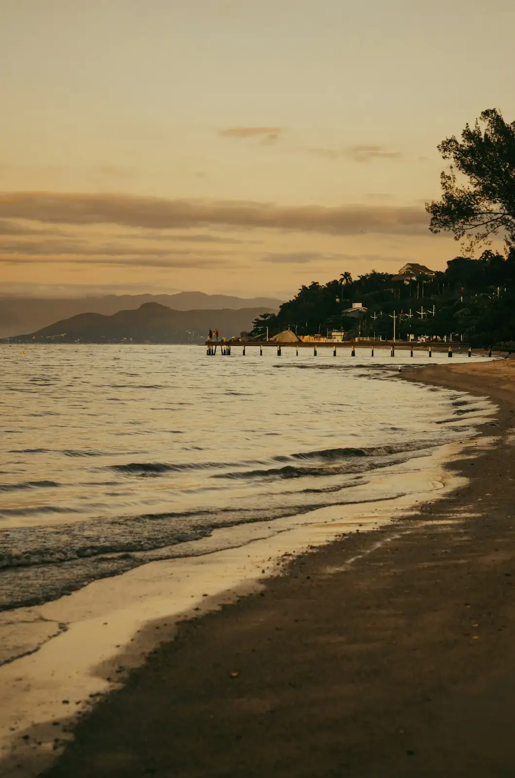 Praia de baía ao pôr do sol com barcos de pesca e árvores na margem