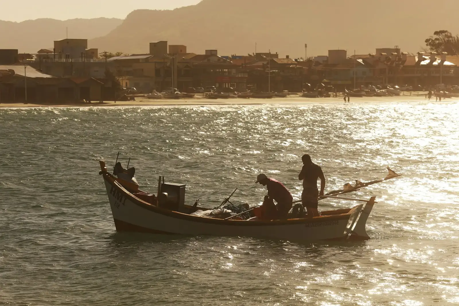 Pescadores numa canoa na baía, contra o sol do fim de tarde