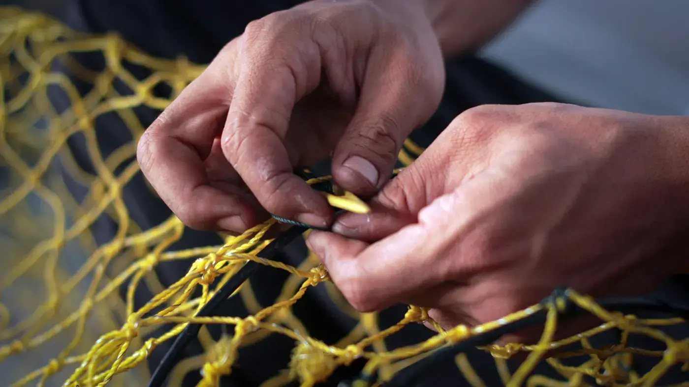 Mãos remendando uma rede de pesca amarela