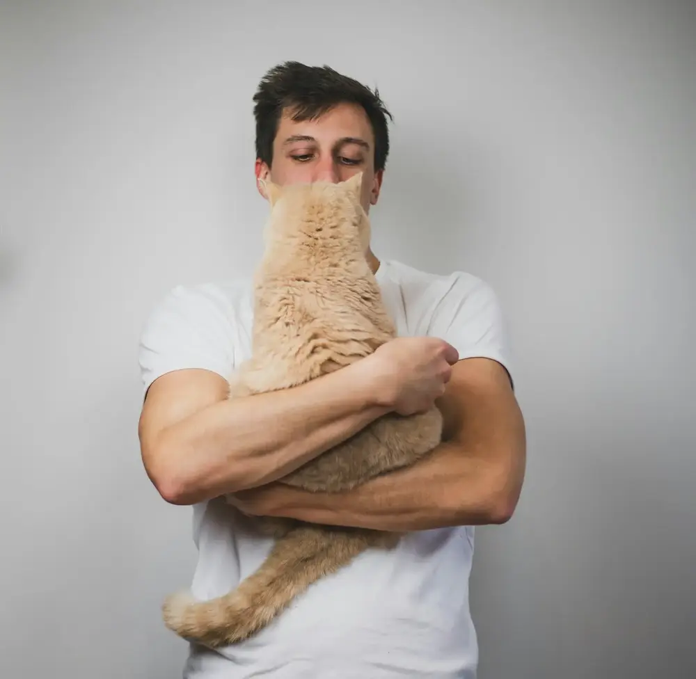 Homem abraçando um gato laranja contra o peito