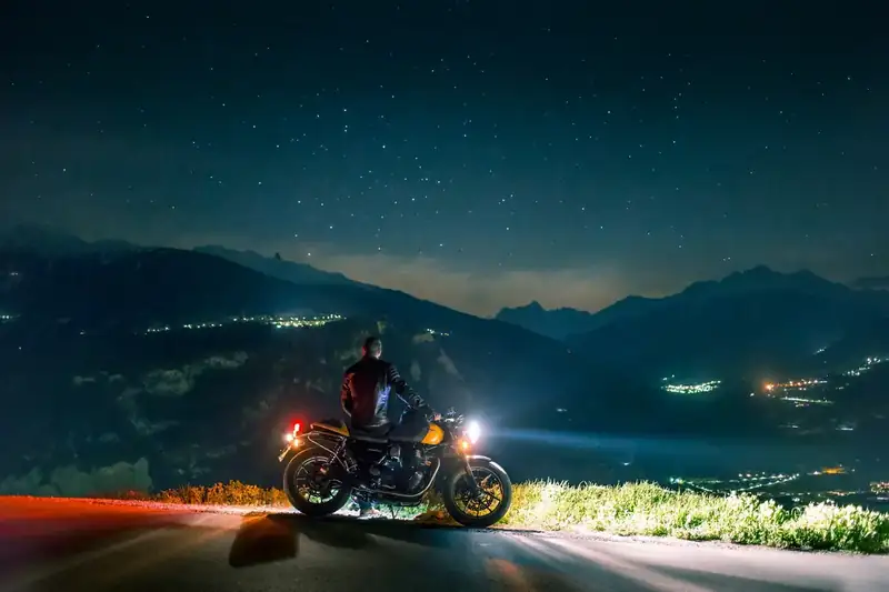 Motociclista parado com o farol aceso numa estrada de serra à noite